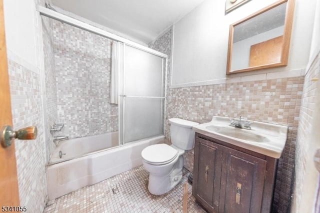 bathroom with tile patterned flooring, toilet, bath / shower combo with glass door, vanity, and tile walls