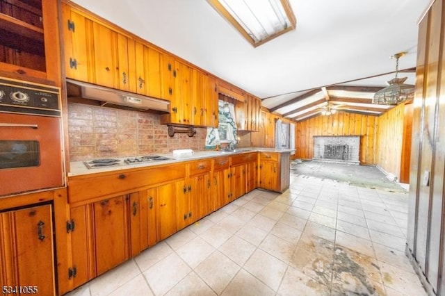 kitchen featuring lofted ceiling, wall oven, wood walls, stainless steel stovetop, and under cabinet range hood