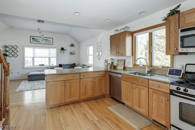 kitchen featuring stainless steel appliances, a peninsula, a sink, vaulted ceiling, and light wood finished floors