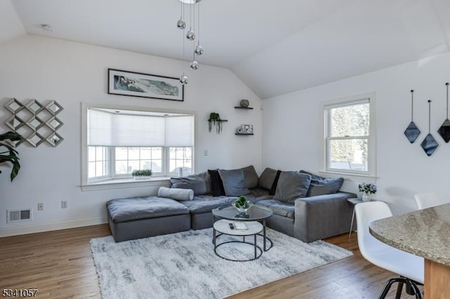 living area with lofted ceiling, baseboards, visible vents, and wood finished floors