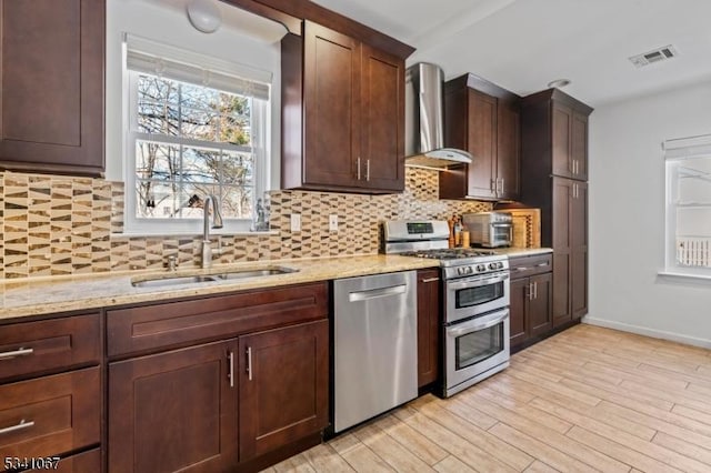 kitchen featuring a sink, visible vents, wall chimney range hood, appliances with stainless steel finishes, and light stone countertops