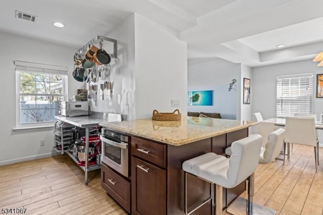 kitchen featuring light wood-style floors, visible vents, stainless steel oven, and light stone counters