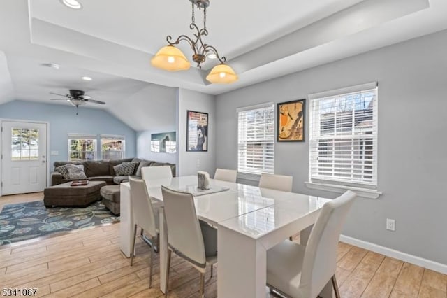 dining room with light wood-type flooring, a tray ceiling, a notable chandelier, and baseboards