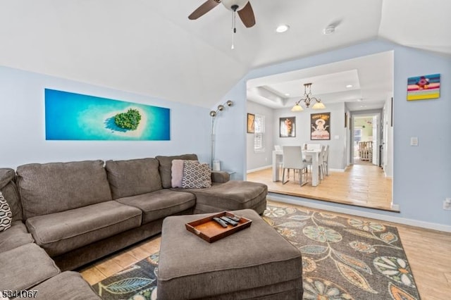 living room featuring baseboards, light wood-style flooring, a tray ceiling, ceiling fan with notable chandelier, and recessed lighting