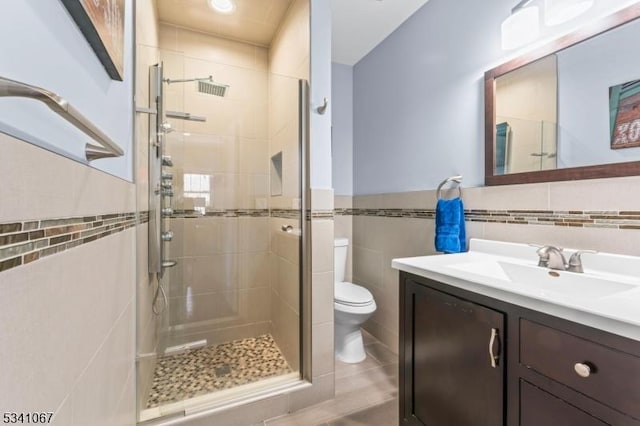 bathroom with a stall shower, toilet, a wainscoted wall, vanity, and tile walls