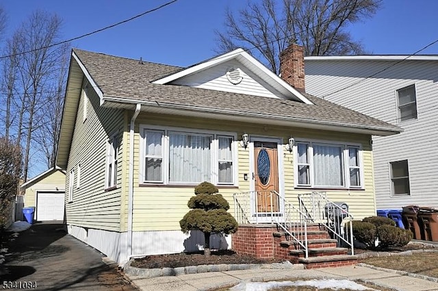 view of front of house with a shingled roof, an outdoor structure, a chimney, and a garage