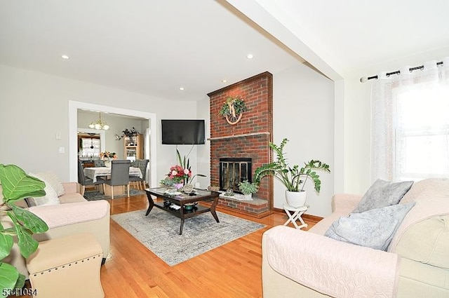 living room with recessed lighting, a brick fireplace, an inviting chandelier, and wood finished floors