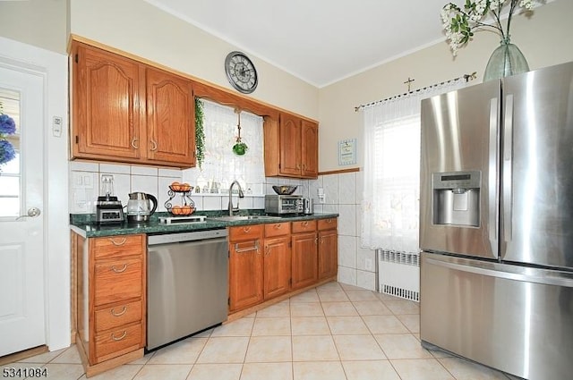 kitchen with light tile patterned floors, stainless steel appliances, radiator, brown cabinetry, and dark countertops