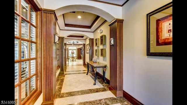 hall with arched walkways, a tray ceiling, baseboards, and crown molding