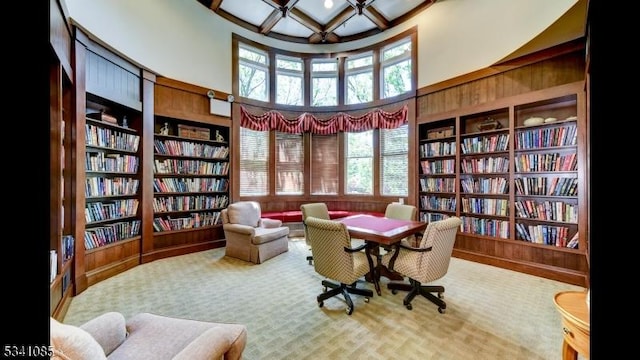 living area with built in shelves, a high ceiling, wall of books, coffered ceiling, and beamed ceiling