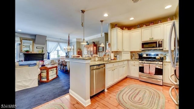 kitchen with appliances with stainless steel finishes, open floor plan, a peninsula, light wood-type flooring, and a sink