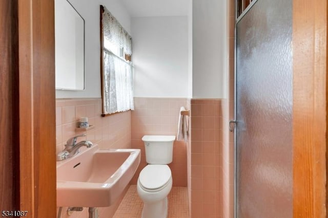 full bathroom with a shower with shower door, toilet, a wainscoted wall, a sink, and tile walls