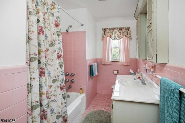 full bath featuring a wainscoted wall, shower / bath combination with curtain, vanity, and tile walls