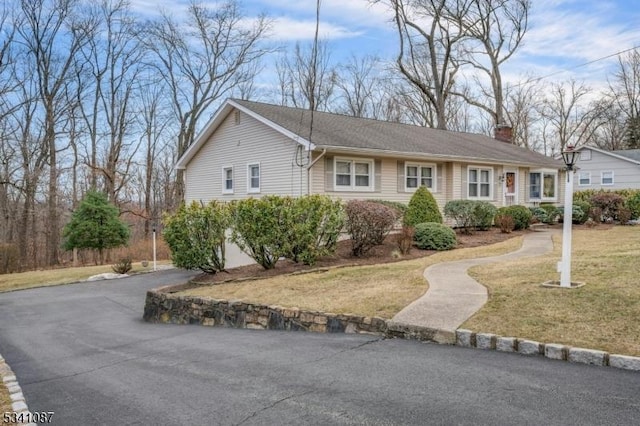 ranch-style house with driveway, a chimney, and a front lawn