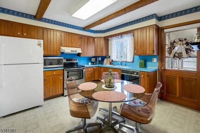 kitchen featuring appliances with stainless steel finishes, brown cabinetry, under cabinet range hood, and light floors