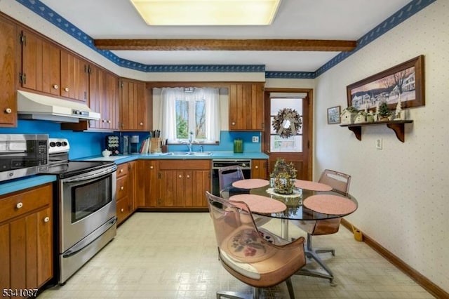 kitchen with under cabinet range hood, stainless steel appliances, a sink, brown cabinets, and wallpapered walls