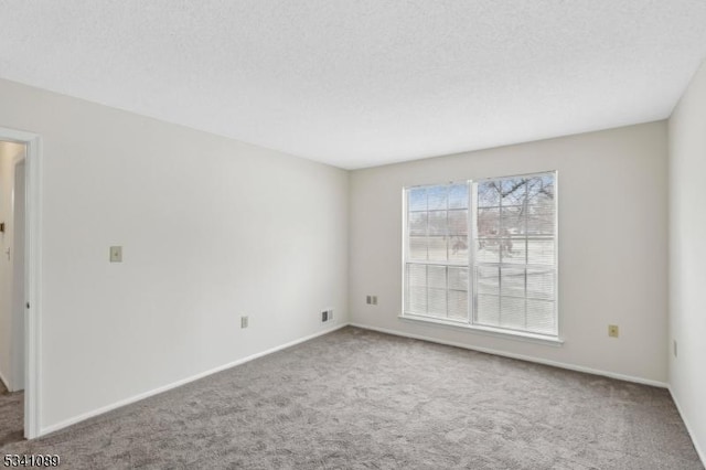 carpeted spare room with baseboards, visible vents, and a textured ceiling