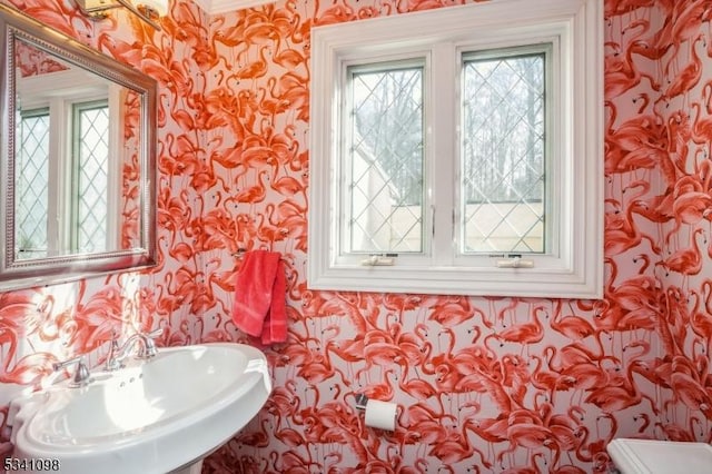 half bathroom with a sink, toilet, and wallpapered walls