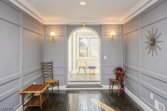 interior space with crown molding, arched walkways, a decorative wall, and wood finished floors