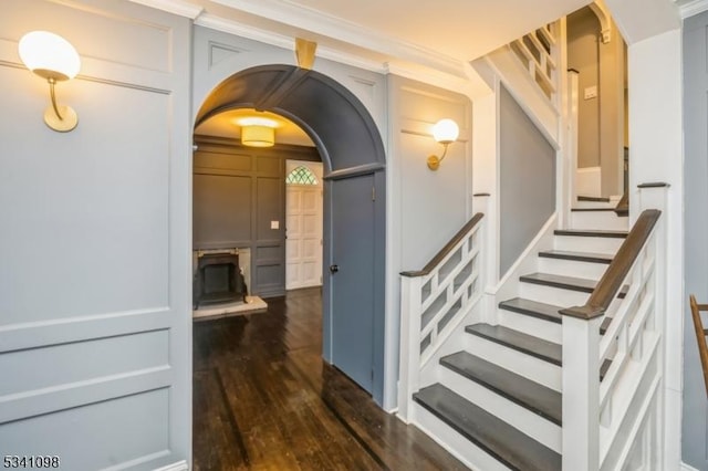 staircase featuring arched walkways and wood finished floors