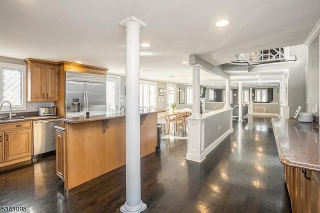 kitchen featuring decorative columns, brown cabinets, dark wood-type flooring, stainless steel appliances, and a sink