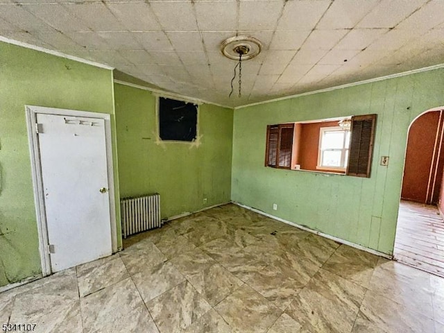 unfurnished room featuring ornamental molding, arched walkways, and radiator