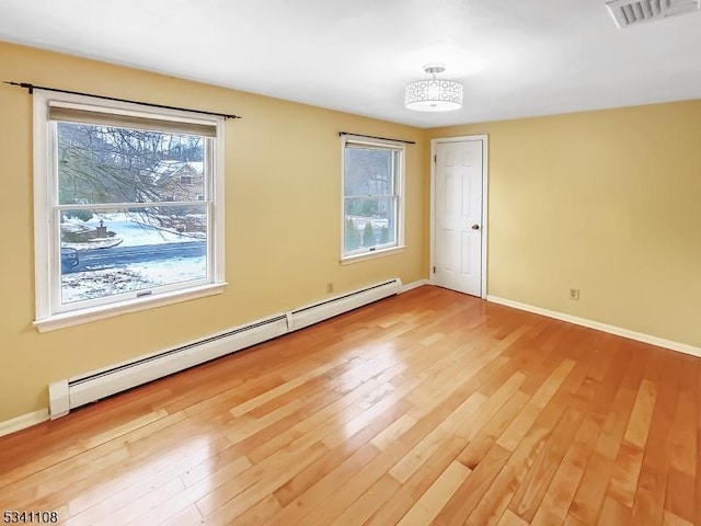 empty room featuring a baseboard heating unit, visible vents, light wood-style flooring, and baseboards