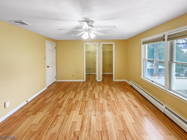 unfurnished bedroom featuring a walk in closet, a baseboard radiator, visible vents, light wood-style flooring, and baseboards