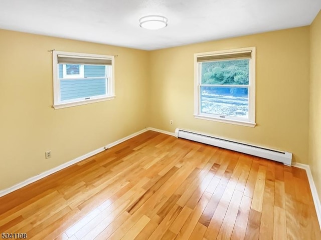 empty room featuring light wood-type flooring, a baseboard radiator, and baseboards