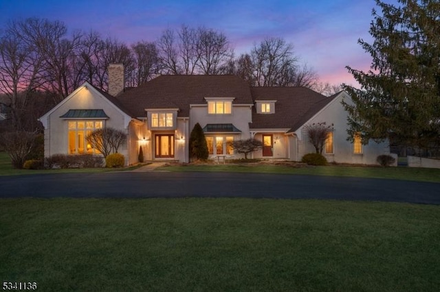 view of front of home with aphalt driveway, a front yard, and a chimney