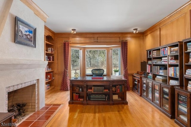 office area with crown molding, light wood-style floors, a fireplace, and built in features