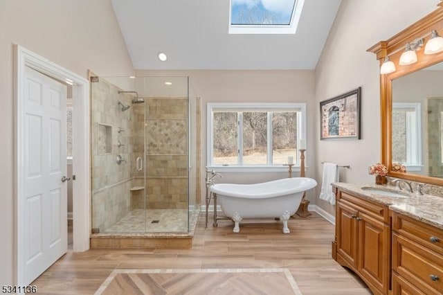 full bathroom featuring lofted ceiling with skylight, vanity, a freestanding bath, and a stall shower