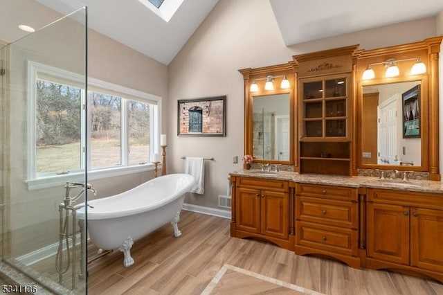 bathroom with double vanity, vaulted ceiling with skylight, a soaking tub, wood finished floors, and a sink