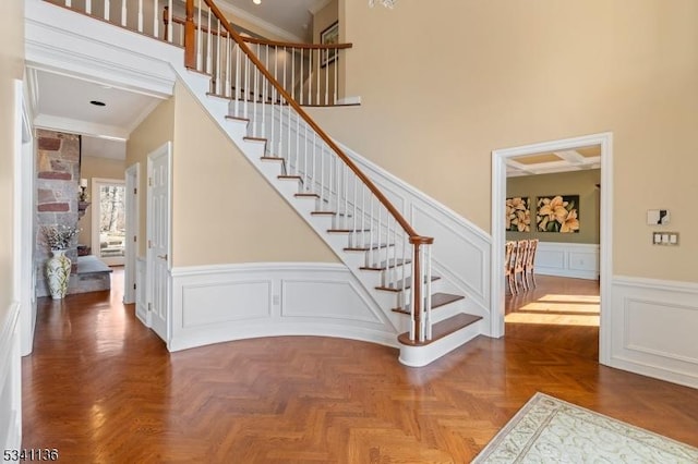 staircase featuring crown molding, a wainscoted wall, a decorative wall, and a high ceiling