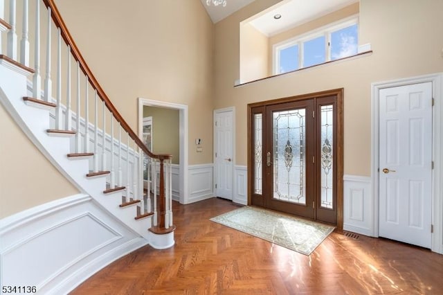 foyer with a wainscoted wall, stairs, a towering ceiling, and a decorative wall