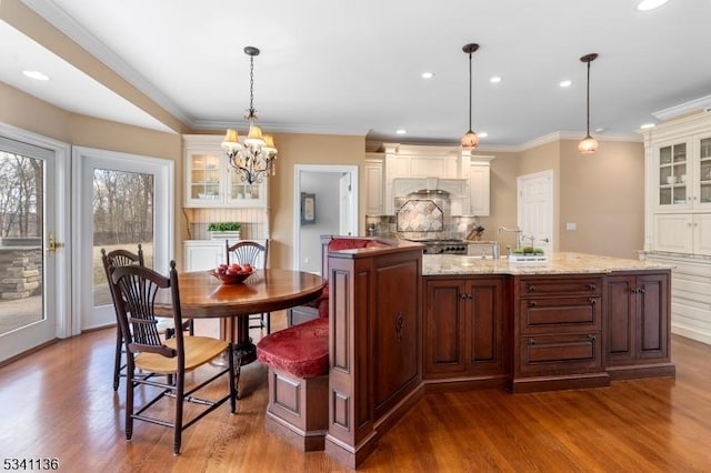 kitchen with wood finished floors, ornamental molding, backsplash, range, and glass insert cabinets