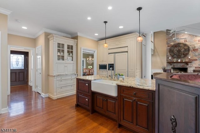 kitchen featuring a stone fireplace, paneled built in refrigerator, wood finished floors, a sink, and crown molding