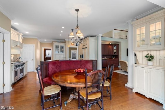 dining area featuring a notable chandelier, recessed lighting, crown molding, wood finished floors, and ornate columns