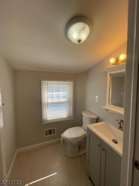 half bath with baseboards, visible vents, toilet, tile patterned floors, and vanity