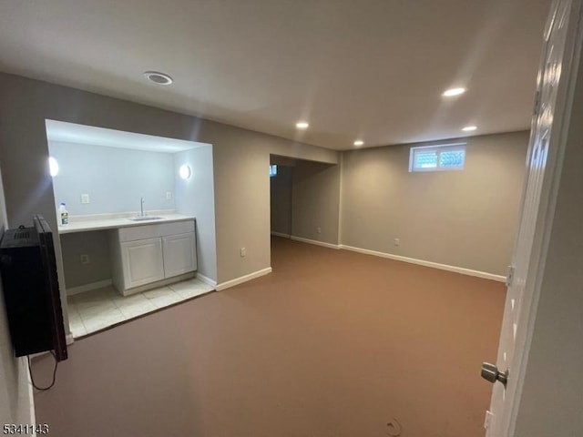 basement with recessed lighting, light colored carpet, a sink, and baseboards