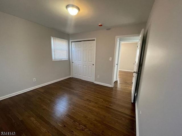 unfurnished bedroom featuring dark wood-type flooring, a closet, and baseboards