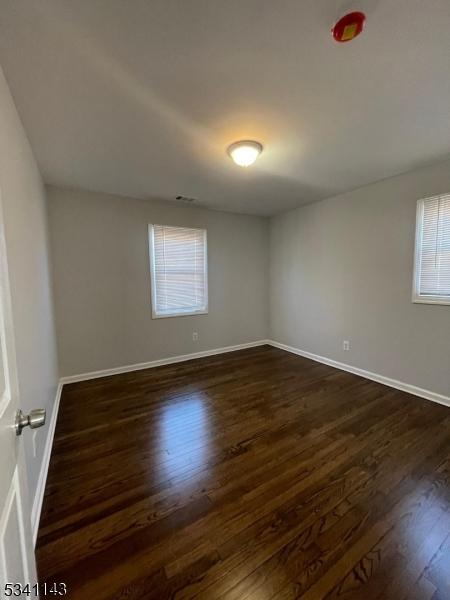 spare room featuring dark wood-style floors, visible vents, and baseboards