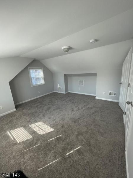 additional living space with lofted ceiling, dark colored carpet, visible vents, and baseboards