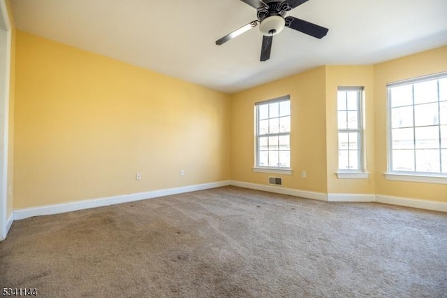 carpeted spare room featuring a ceiling fan, visible vents, a healthy amount of sunlight, and baseboards