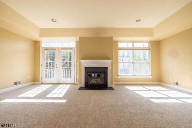 unfurnished living room featuring visible vents, carpet flooring, french doors, and a fireplace with flush hearth