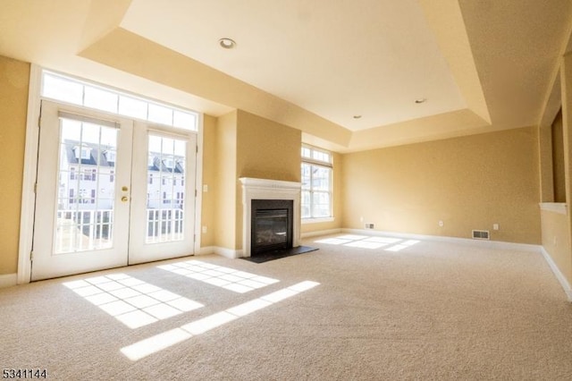 unfurnished living room with a tray ceiling, visible vents, carpet flooring, and french doors