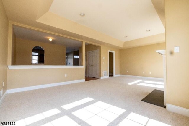 carpeted spare room featuring a tray ceiling, visible vents, and baseboards