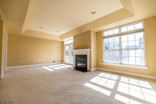 unfurnished living room featuring light carpet, a fireplace with flush hearth, baseboards, and a tray ceiling