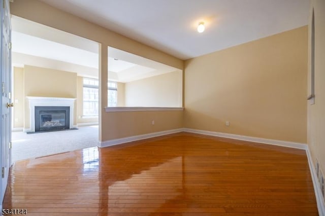 unfurnished living room featuring a glass covered fireplace, baseboards, and wood finished floors