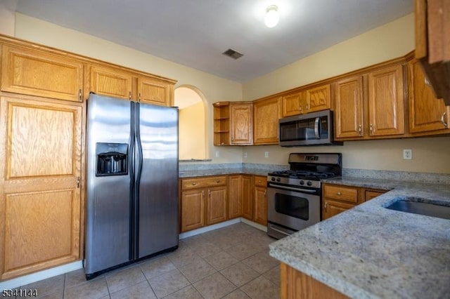 kitchen featuring brown cabinetry, visible vents, open shelves, light tile patterned flooring, and appliances with stainless steel finishes